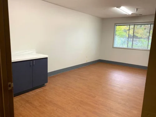 Empty room with wooden flooring, white walls, a cabinet with countertop, and a window with blinds